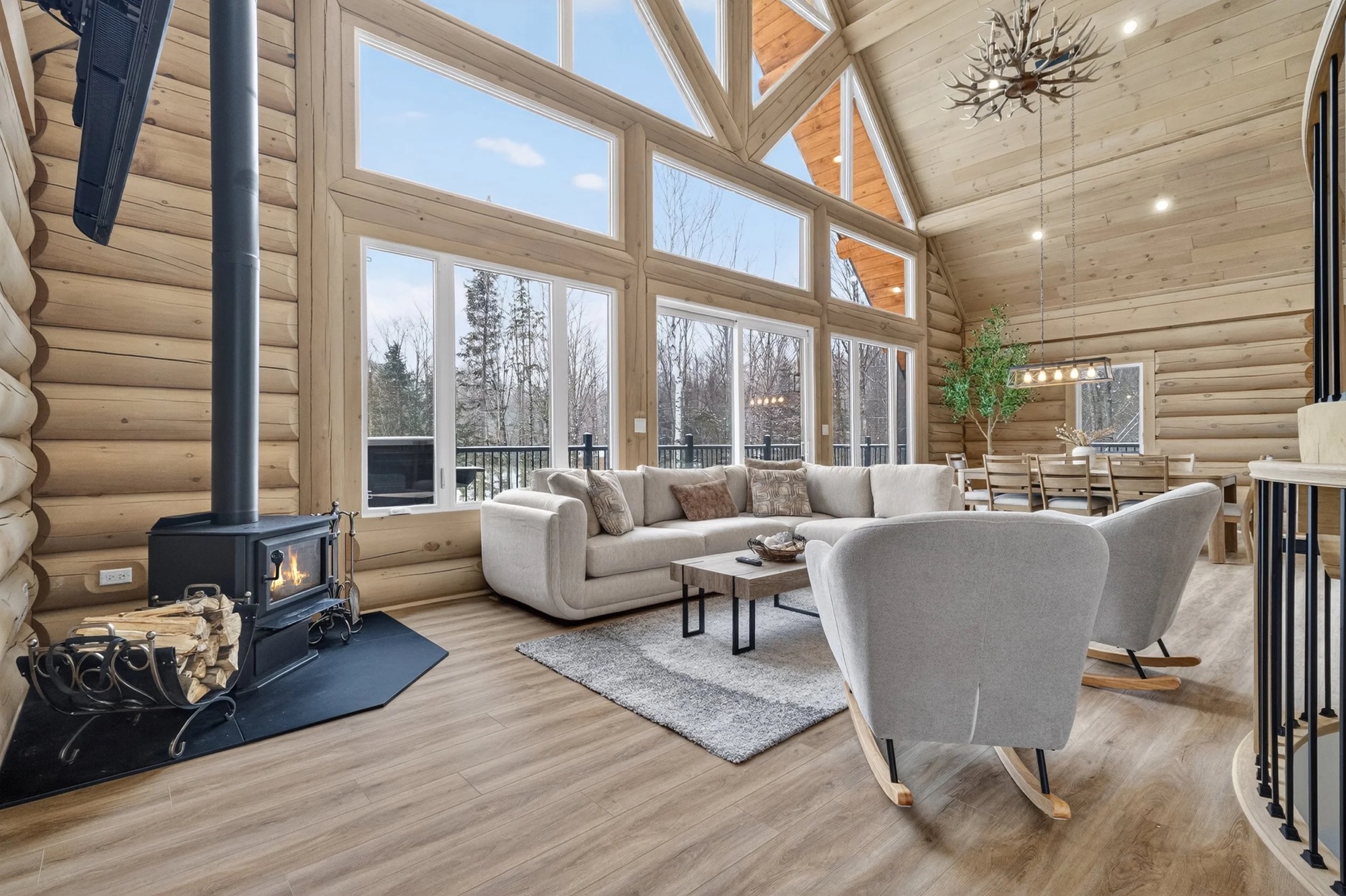 Open living room with log walls, floor-to-ceiling windows and forest views